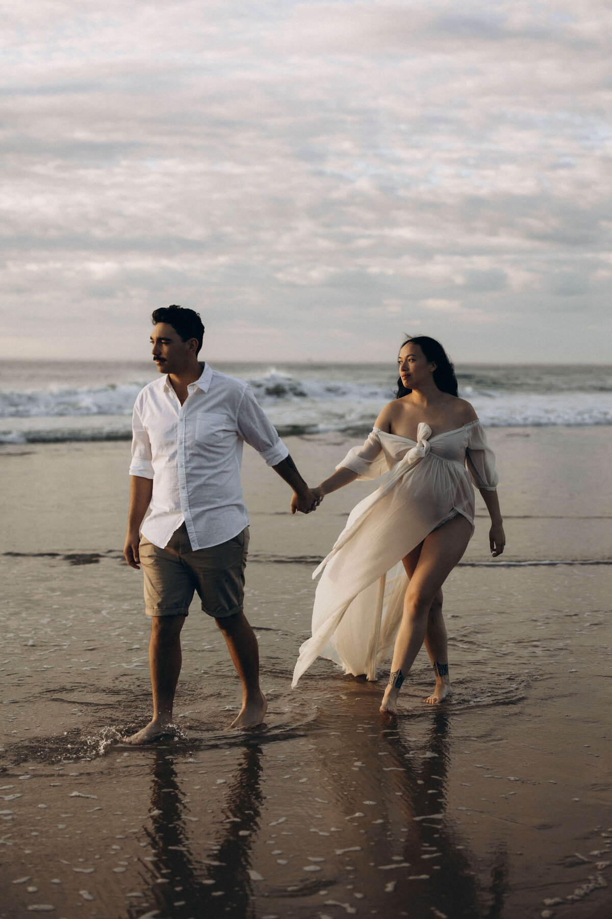 pregnant couple holding hands on the beach