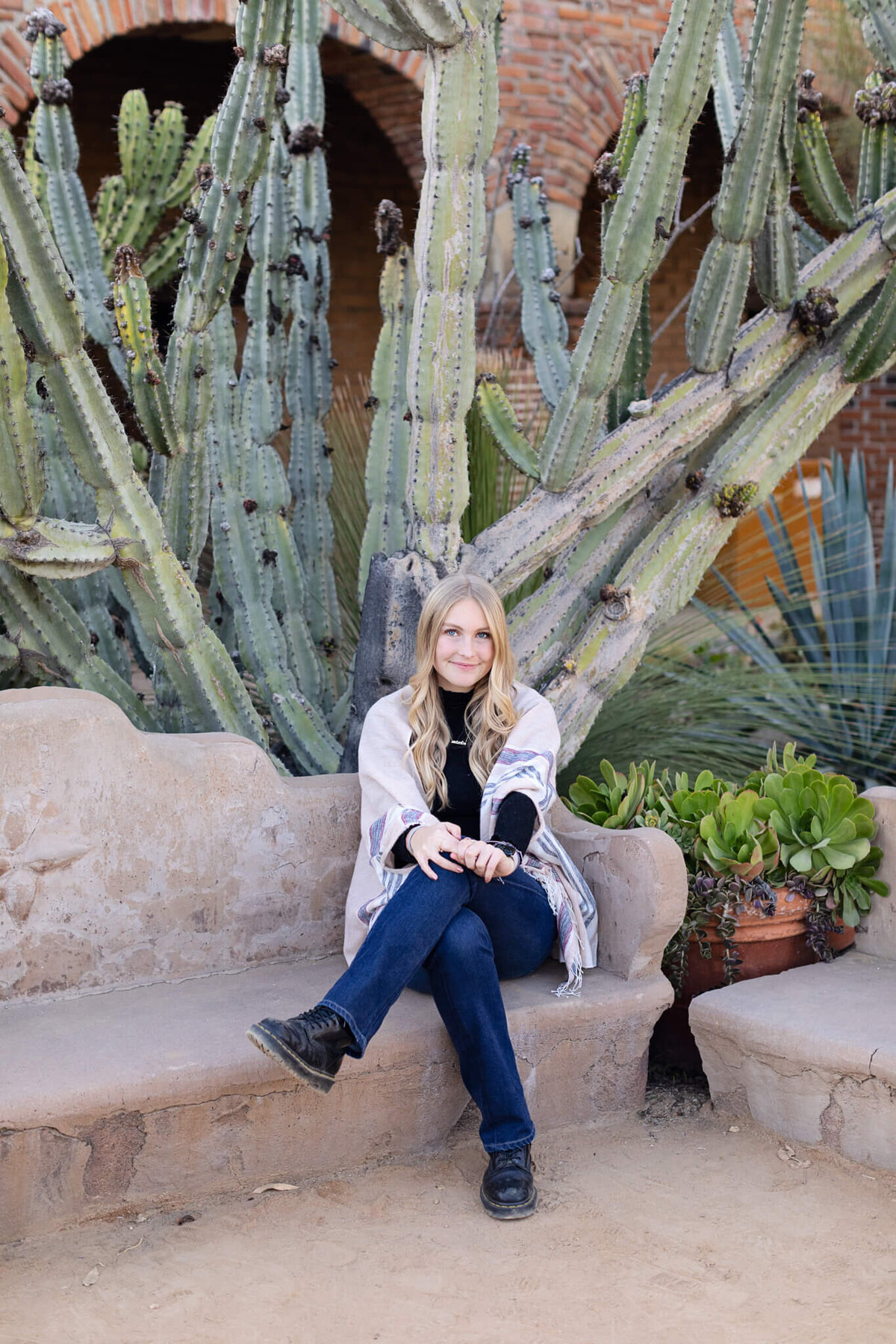 A young blonde woman sitting and crossing her legs at the knees, smiling at the camera.