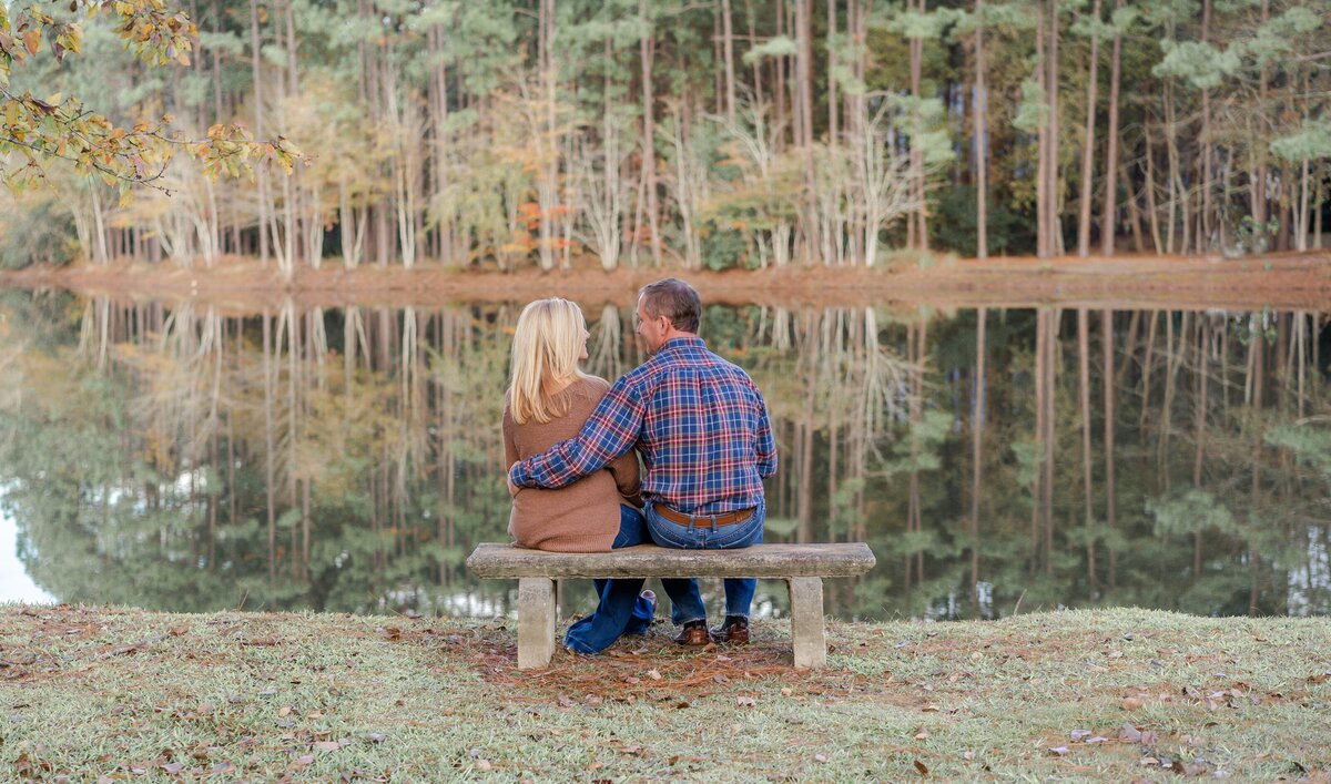 parents sitting on bench at family's pond engaged in conversation at their fall photo shoot