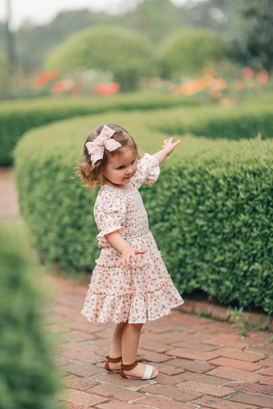 Big sister spinning around near green bushes during family photo session with natural light