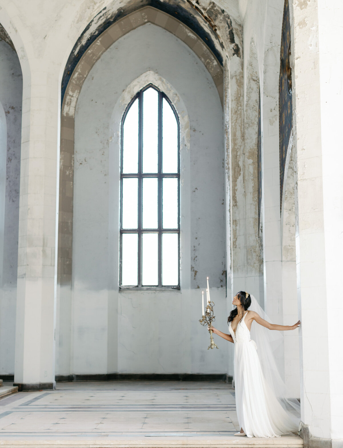 bride with candelabra in beautiful ruins, abandoned cathedral wedding venue in Mediterranean