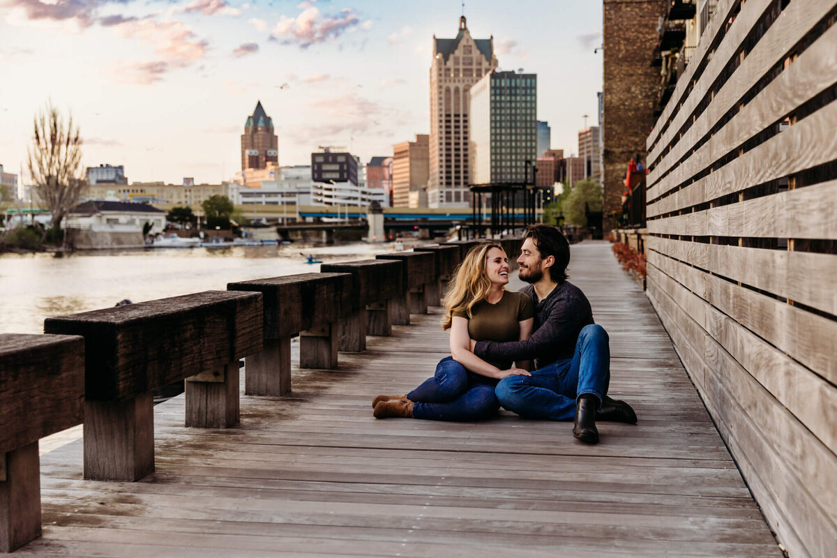 Couple cuddling with Milwaukee skyline in the background for engagement session