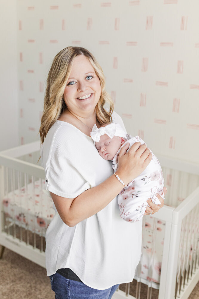 a mom smiling joyfully while holding her newborn baby