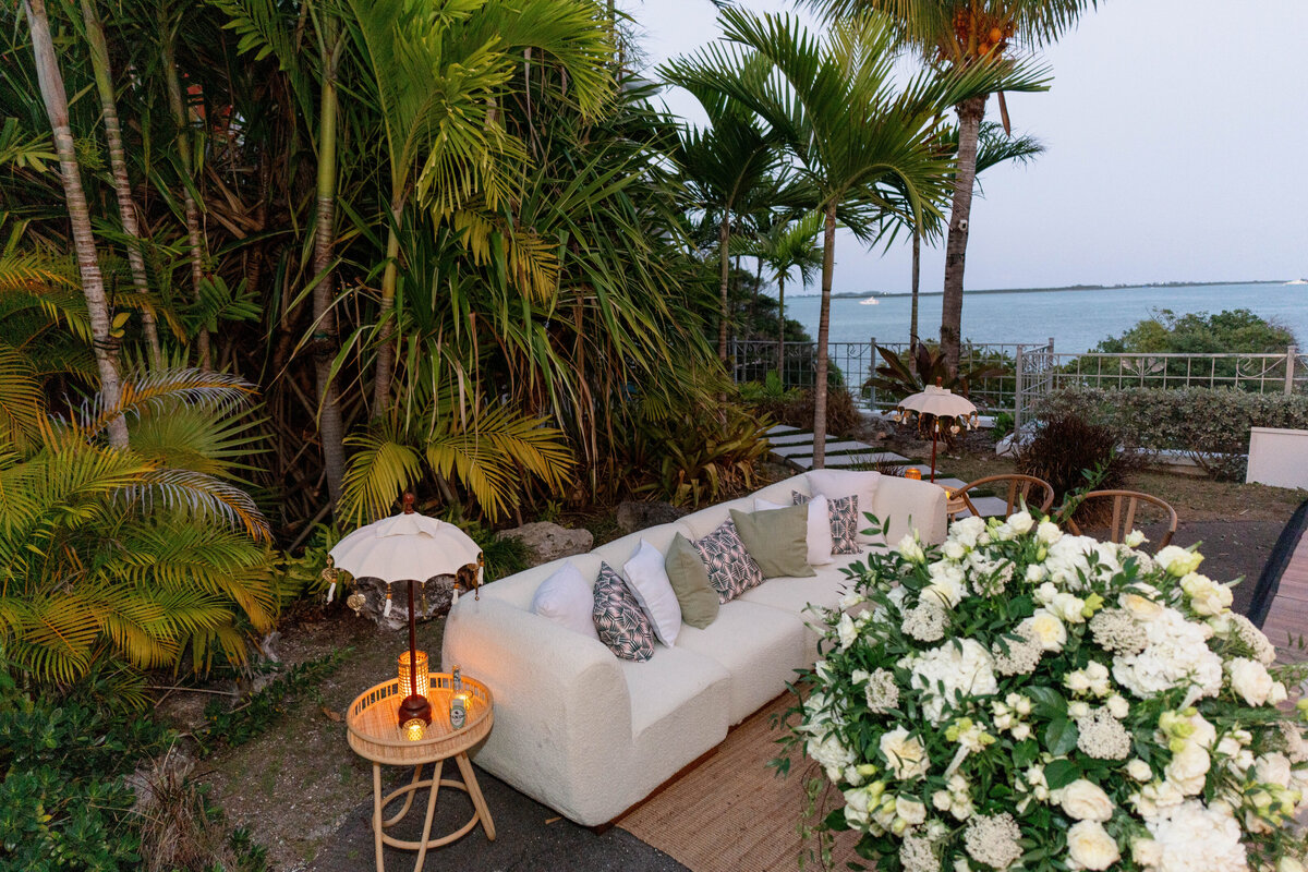 Elegant outdoor wedding lounge with white sofa, tropical greenery, and coastal views at a luxury destination wedding in the Bahamas, photographed by Mari Harsan Studios.