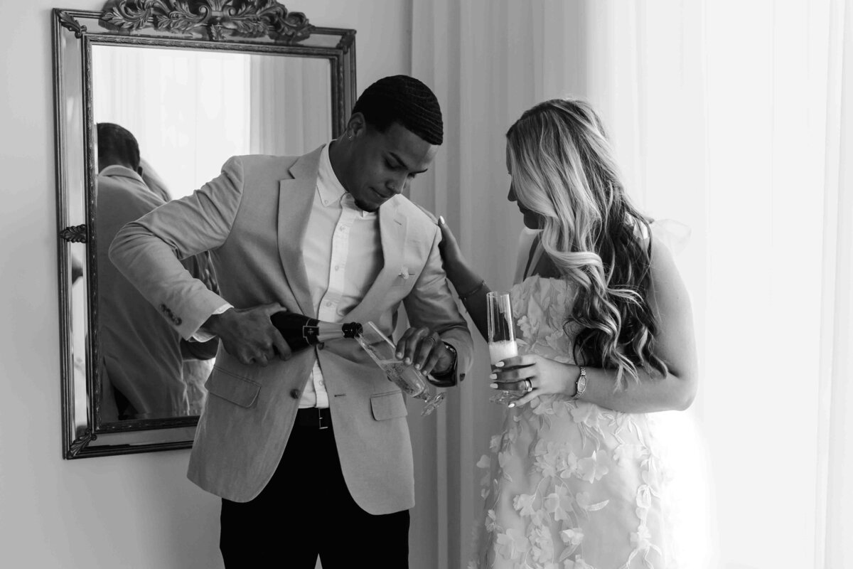 groom pouring champagne for bride in black and white