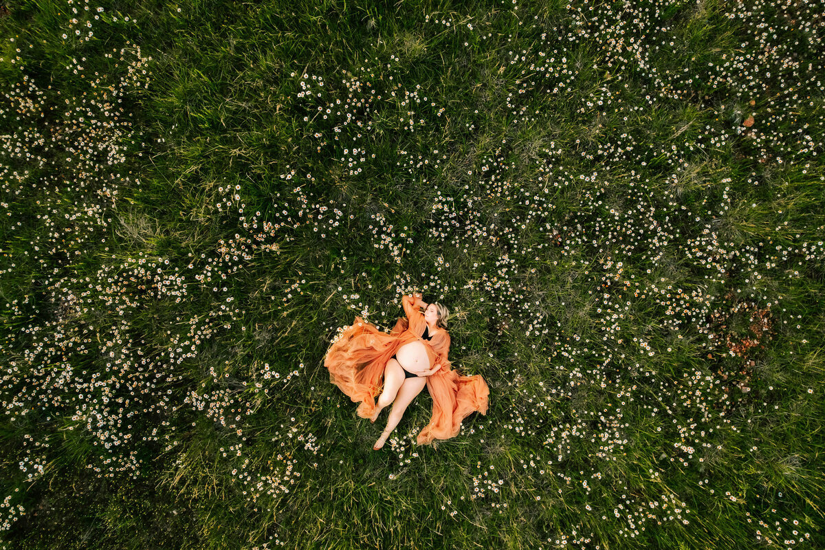 pregnant mom in floral dress hugging belly at a field captured by Branson MO maternity photographer Jessica Kennedy of The XO Photography