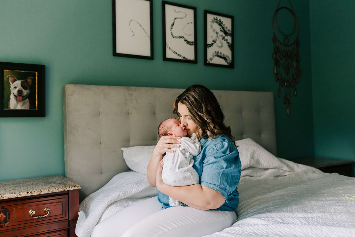 A mother sitting on her bed shushing and kissing her newborn son