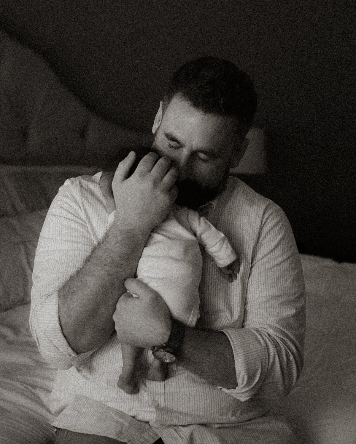Father holding newborn daughter on bed during quiet, in-home newborn session in Temecula.
