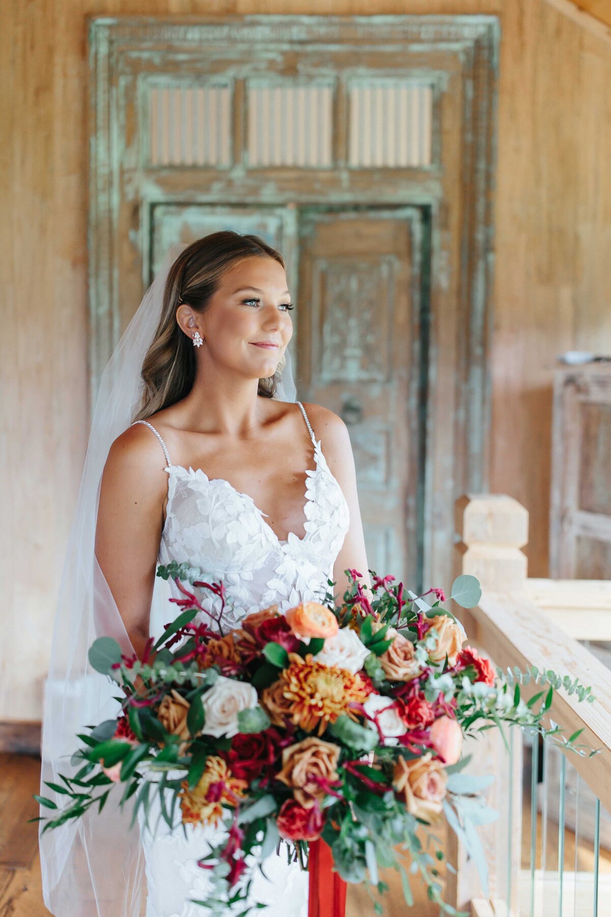 Bride grins into distance with flowers in hand at crooked river venue