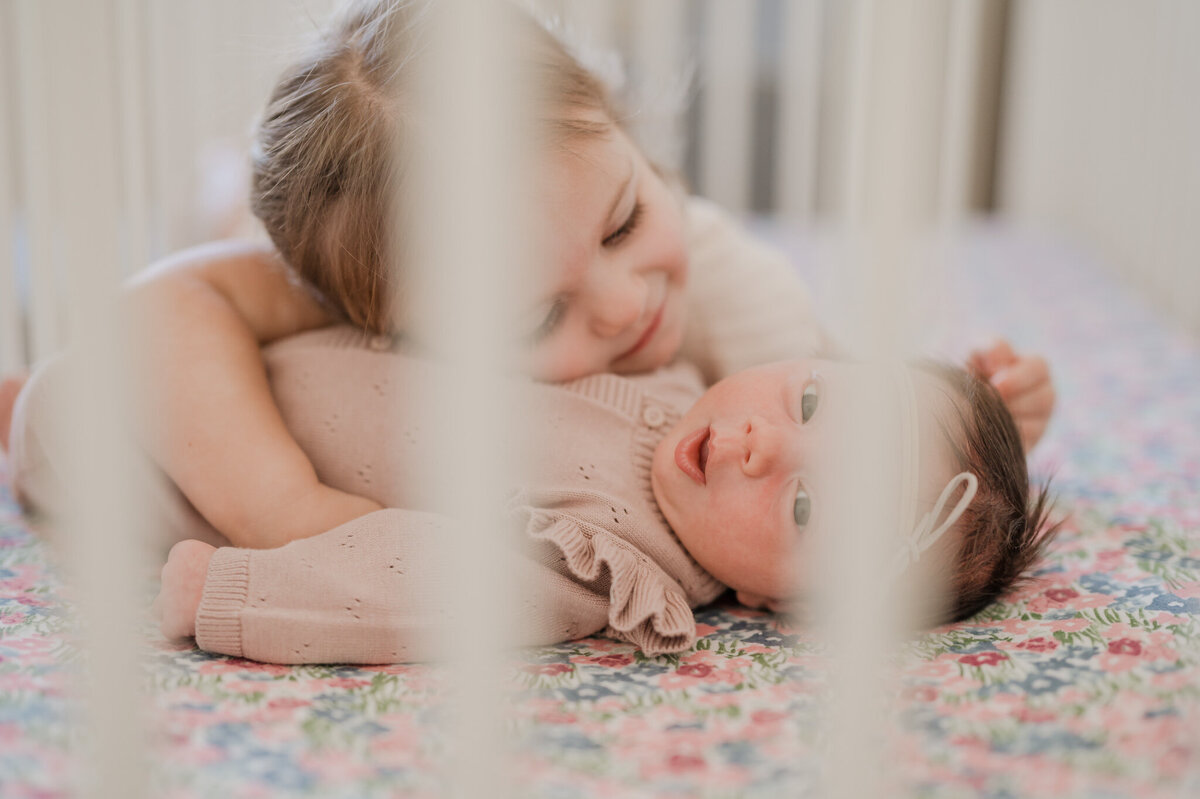 Toddler girl hugs her baby sister in her crib during San Antonio newborn pictures.