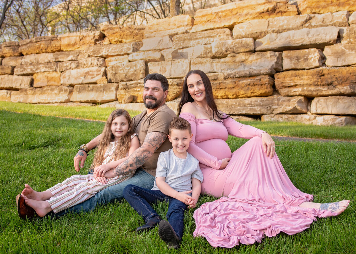 Outdoor family portrait set against a rustic stone wall, featuring parents and two children. Captured in Leawood, Kansas, this setup is ideal for families seeking natural and relaxed photography near Kansas City