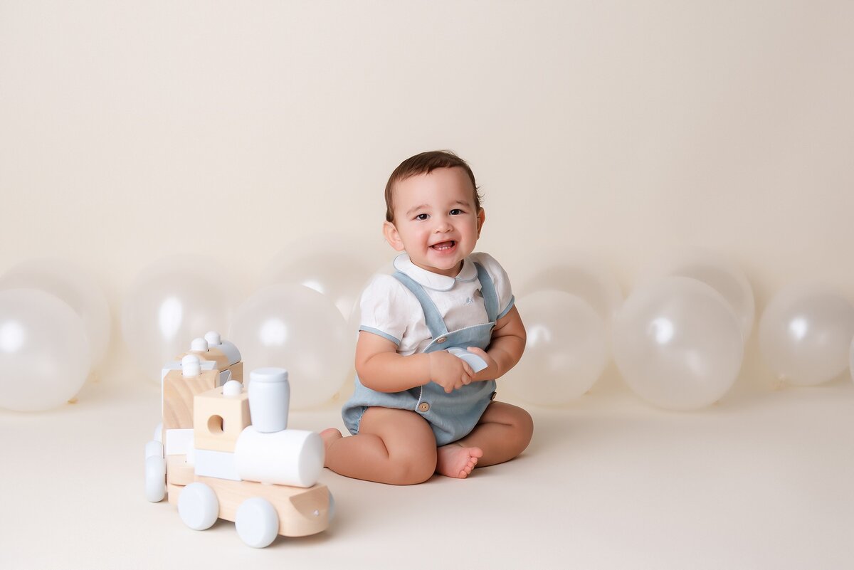 Cake smash photographer near me creates first birthday portrait with balloons in neutral set up.