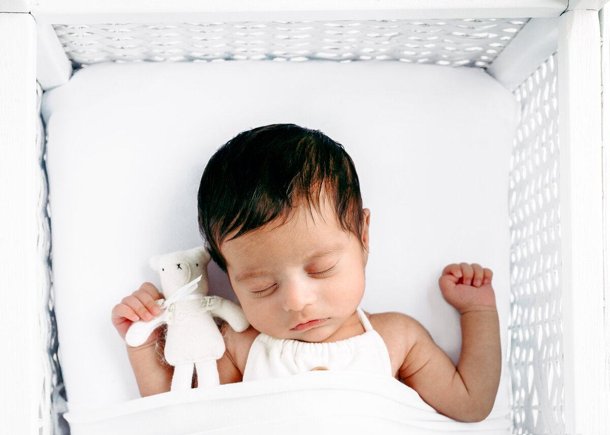Newborn sleeping in a vintage wicker crib with a white teddy in a natural baby-led newborn photography session by Lauren Vanier Photography