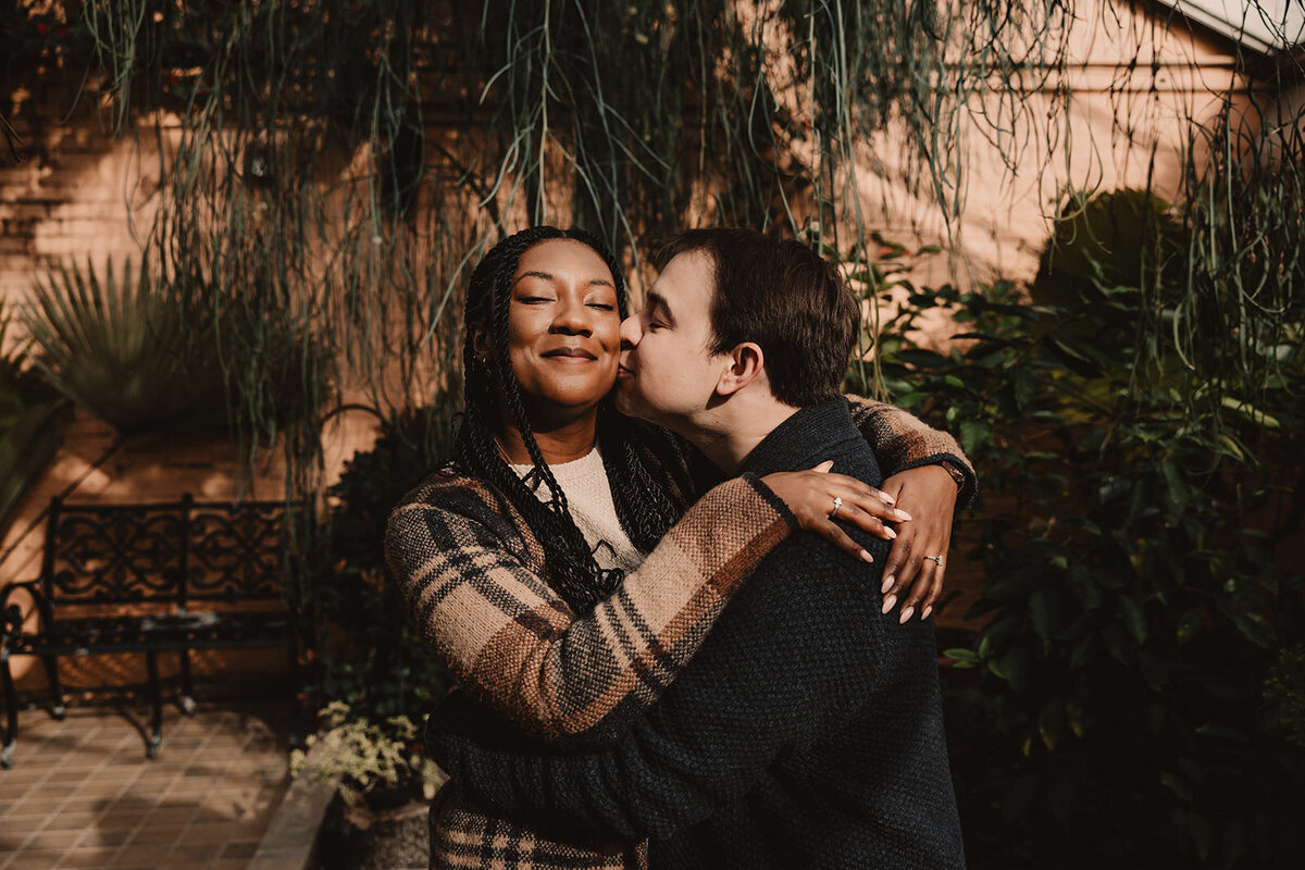 A person hugging their partner and kissing their cheek 