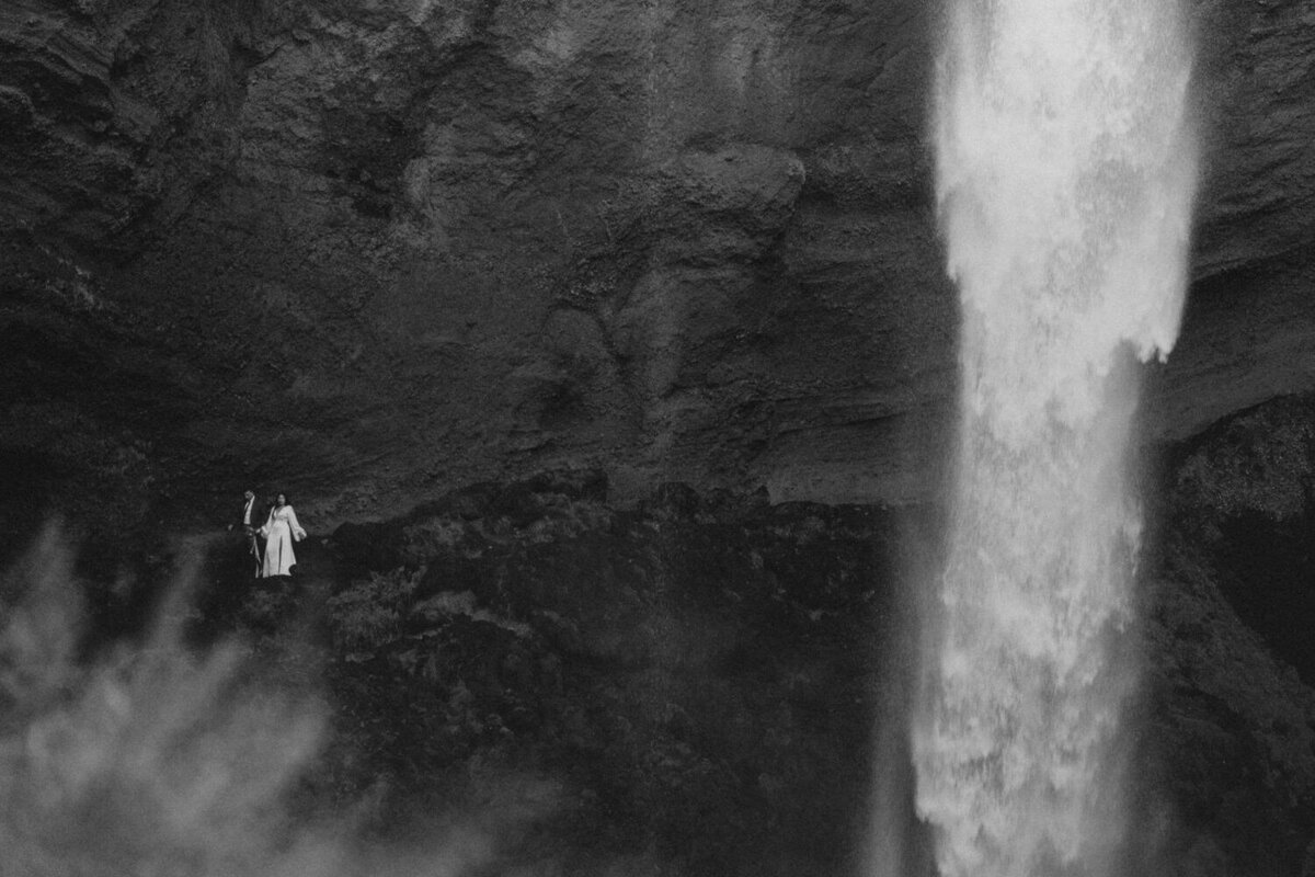 Hand-in-hand, the couple strolls near a peaceful, hidden waterfall in Iceland