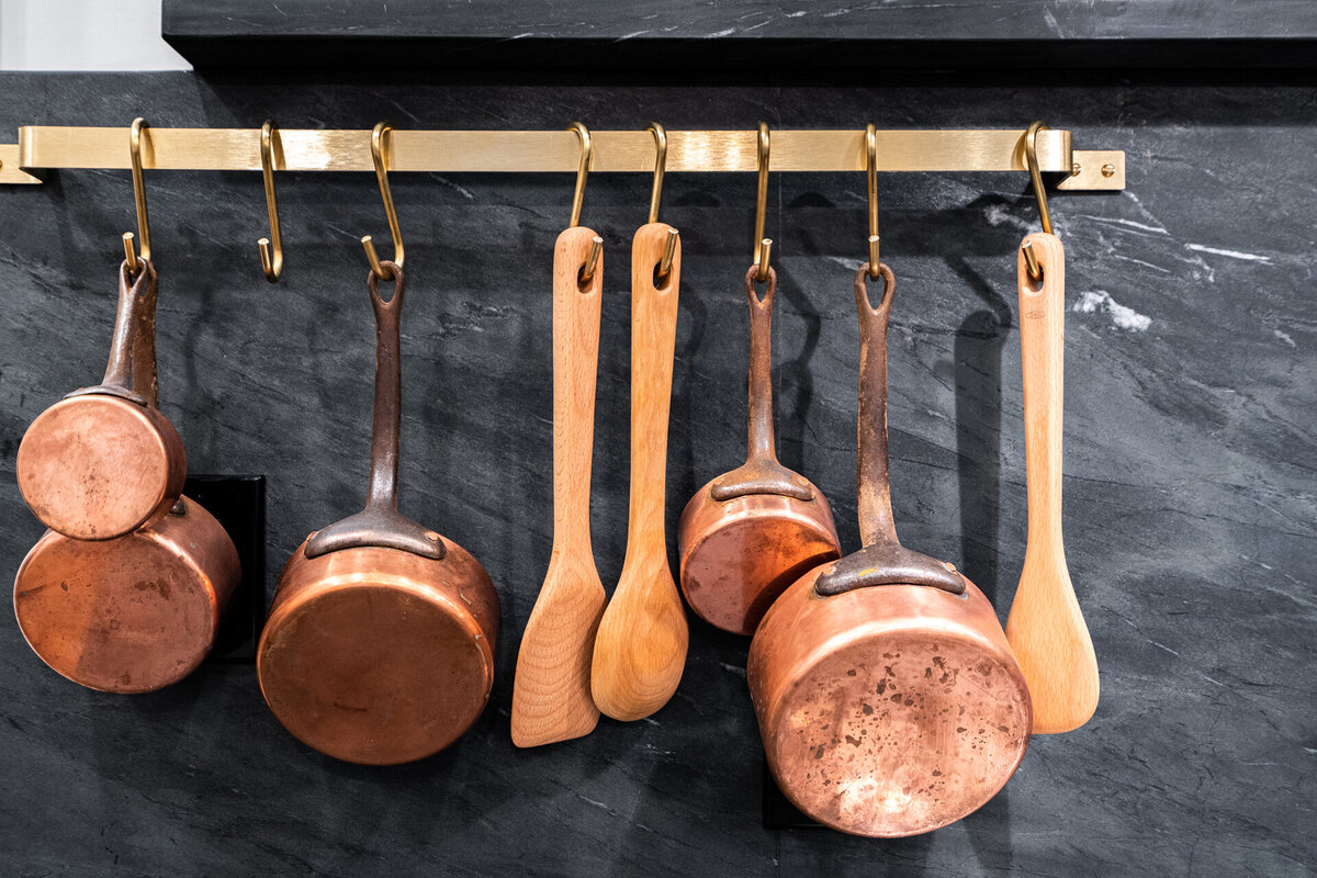 copper pots and wooden spoons hanging from a bar