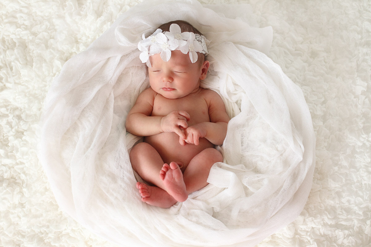 Newborn baby wearing white flowers on her head and sleeping at home newborn photo session in Vancouver British Columbia