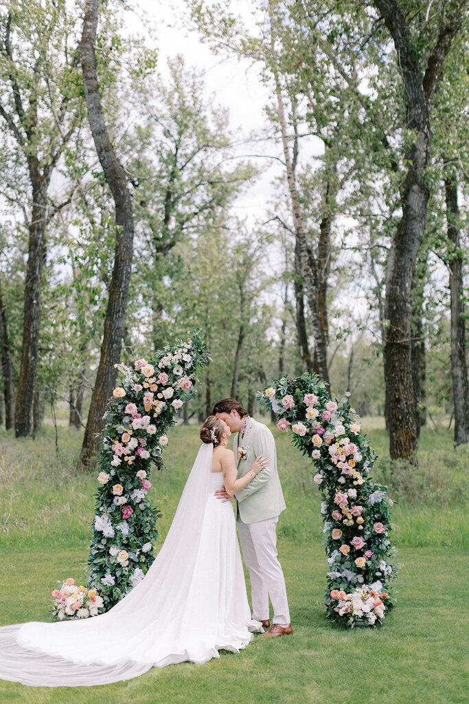 Couple kissing during wedding ceremony at Sugar Pine Island, a romantic wedding venue in Foothills, Alberta, featured on the Brontë Bride Vendor Guide.