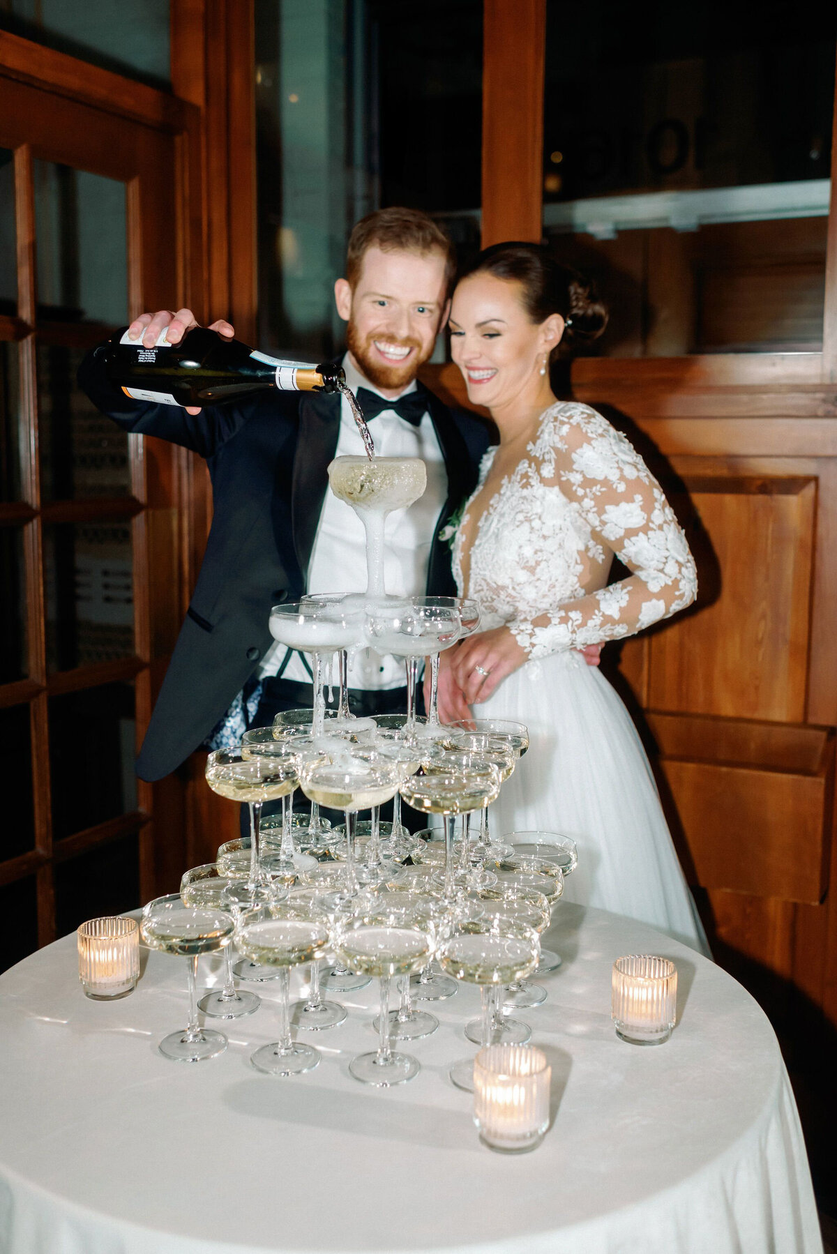 Couple pouring champagne into champagne tower during reception by Kaity Body Photography, film inspired wedding photographer in Calgary, Alberta. Featured on the Bronte Bride Vendor Guide.