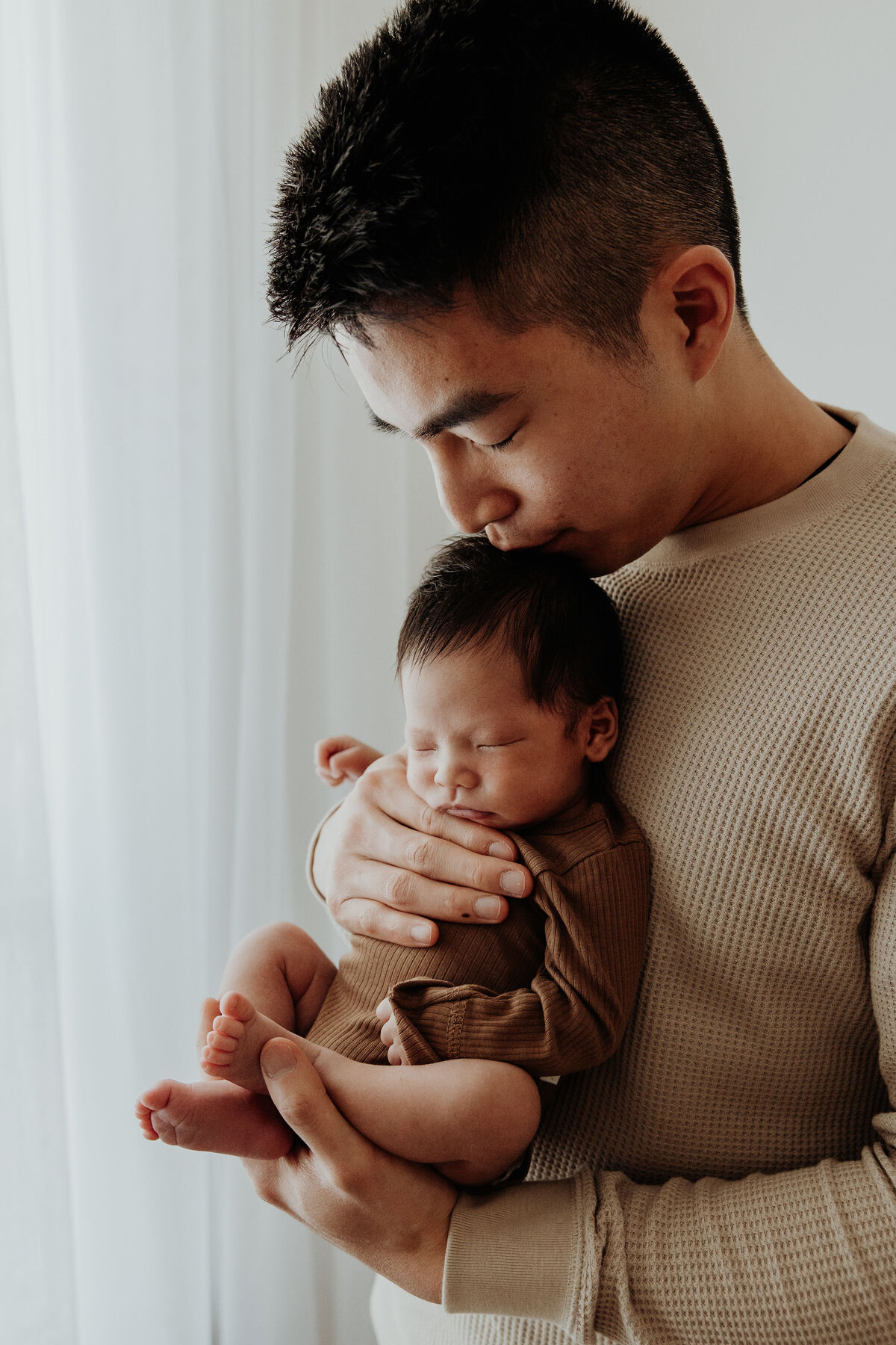 Dad and newborn stand in front of window at newborn studio photography session