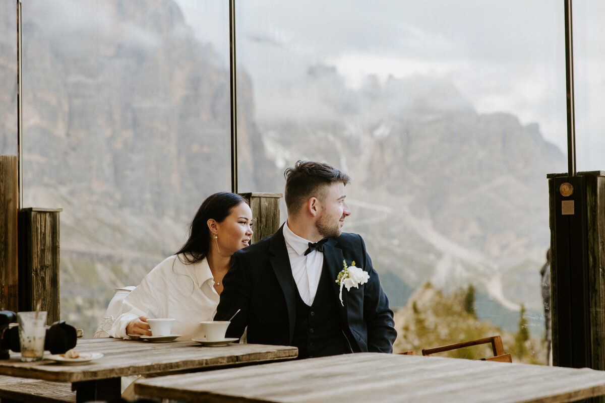 Couple sitting inside mountain hut looking out window.