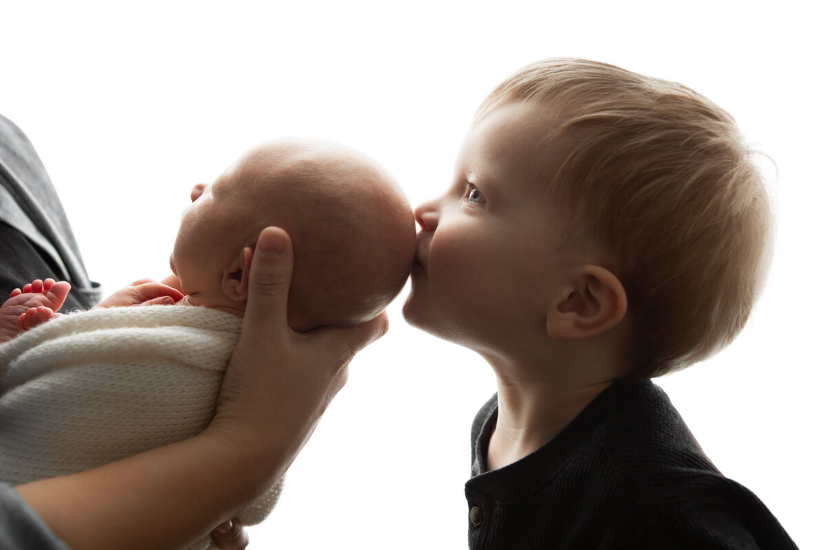 Backlit high contrast photo of big brother kissing newborn baby brother