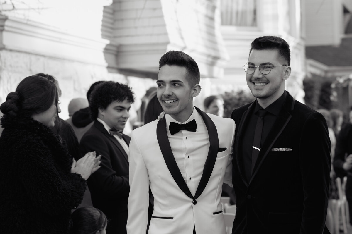 A joyful wedding moment as two grooms walk down the aisle together, captured in an authentic and elegant editorial wedding photograph.