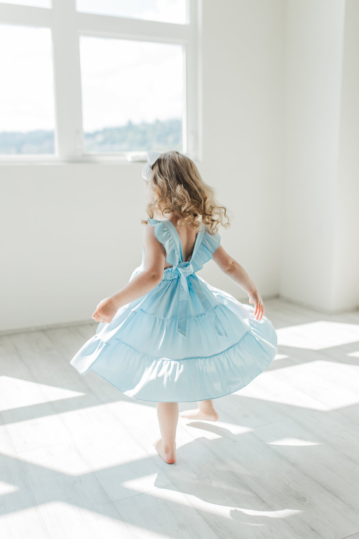 Young girl in blue dress twirling in a sunlit room