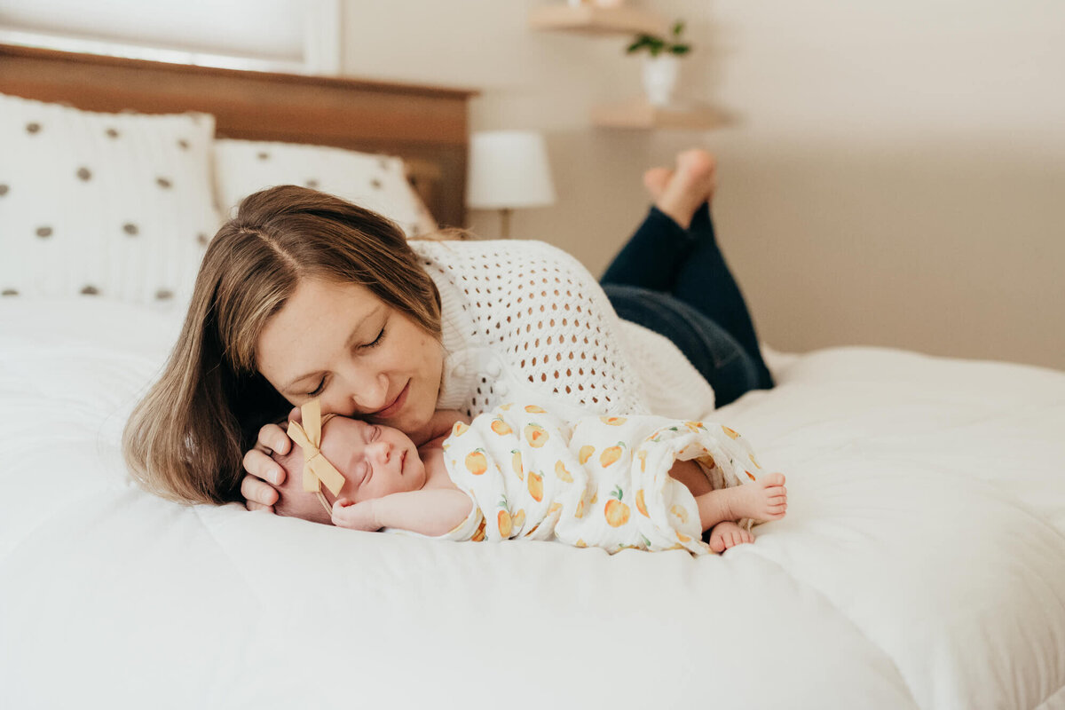 A mother lays next to her sleeping newborn daughter on her bright white bed