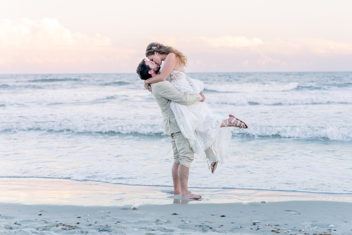 Bride and groom kissing at sunset during topsail beach wedding