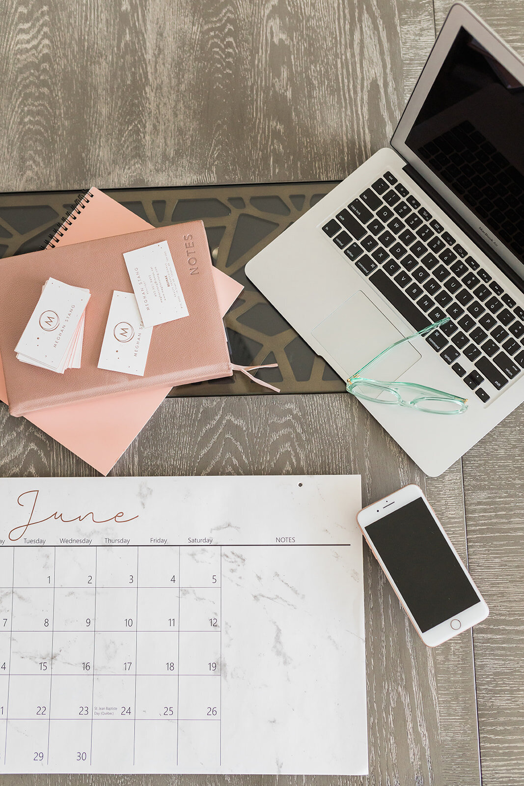 Flatlay photo of calendar, open laptop, iphone and notebook with business cards on top.
