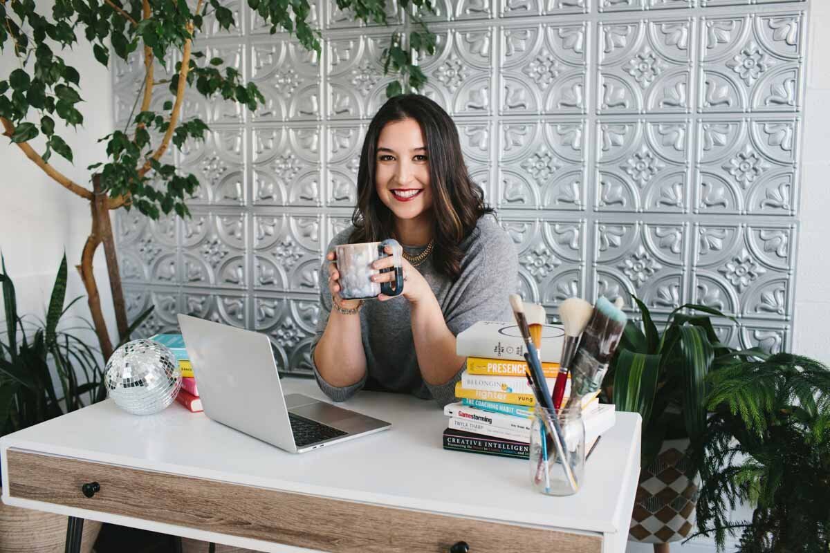 woman sitting at a desk while holding a cup of coffee