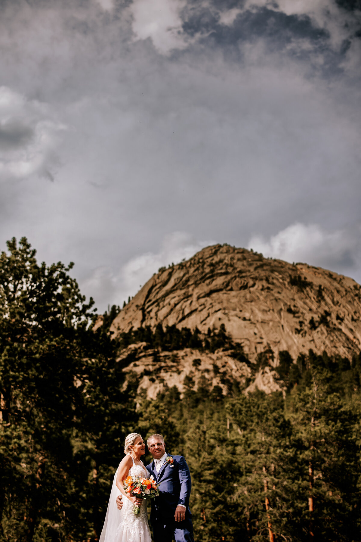 Bride and Groom stand on top of large rock for with a beautiful mountain behind them and ominous skies