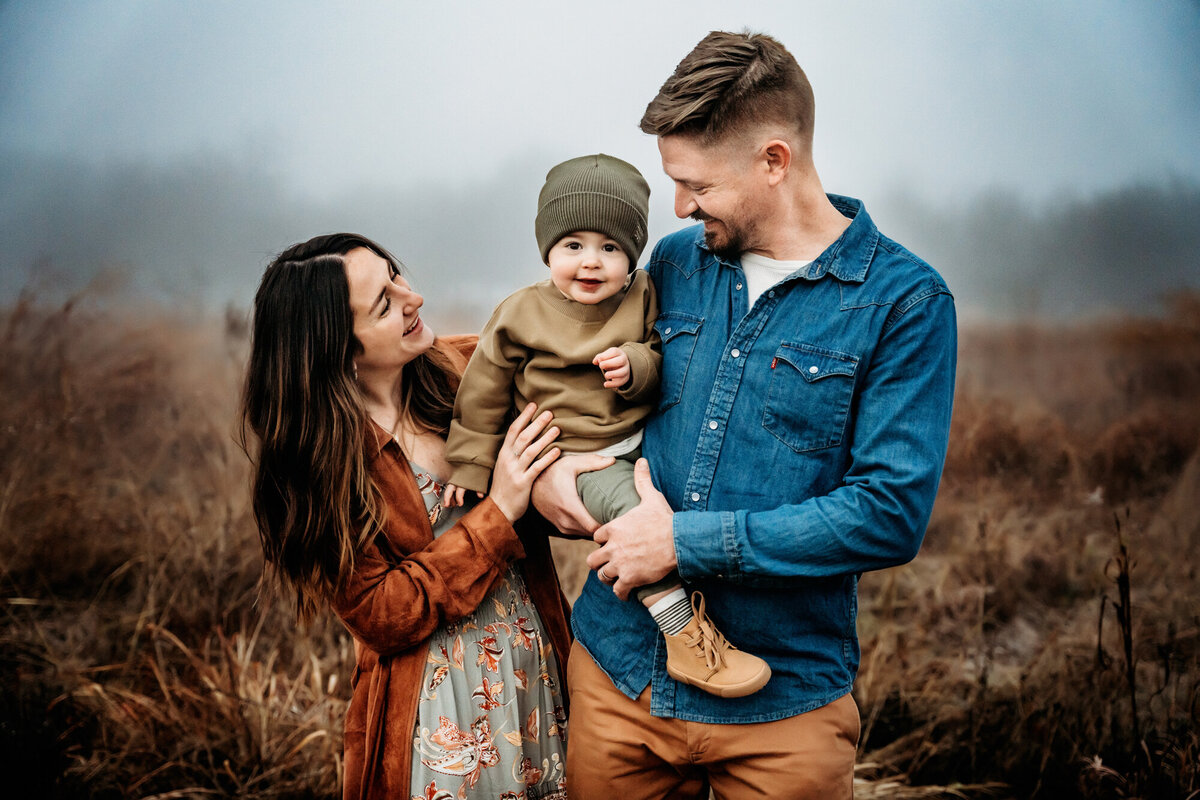 Family Photographer, a mom dad hold their little son in tall dry grass