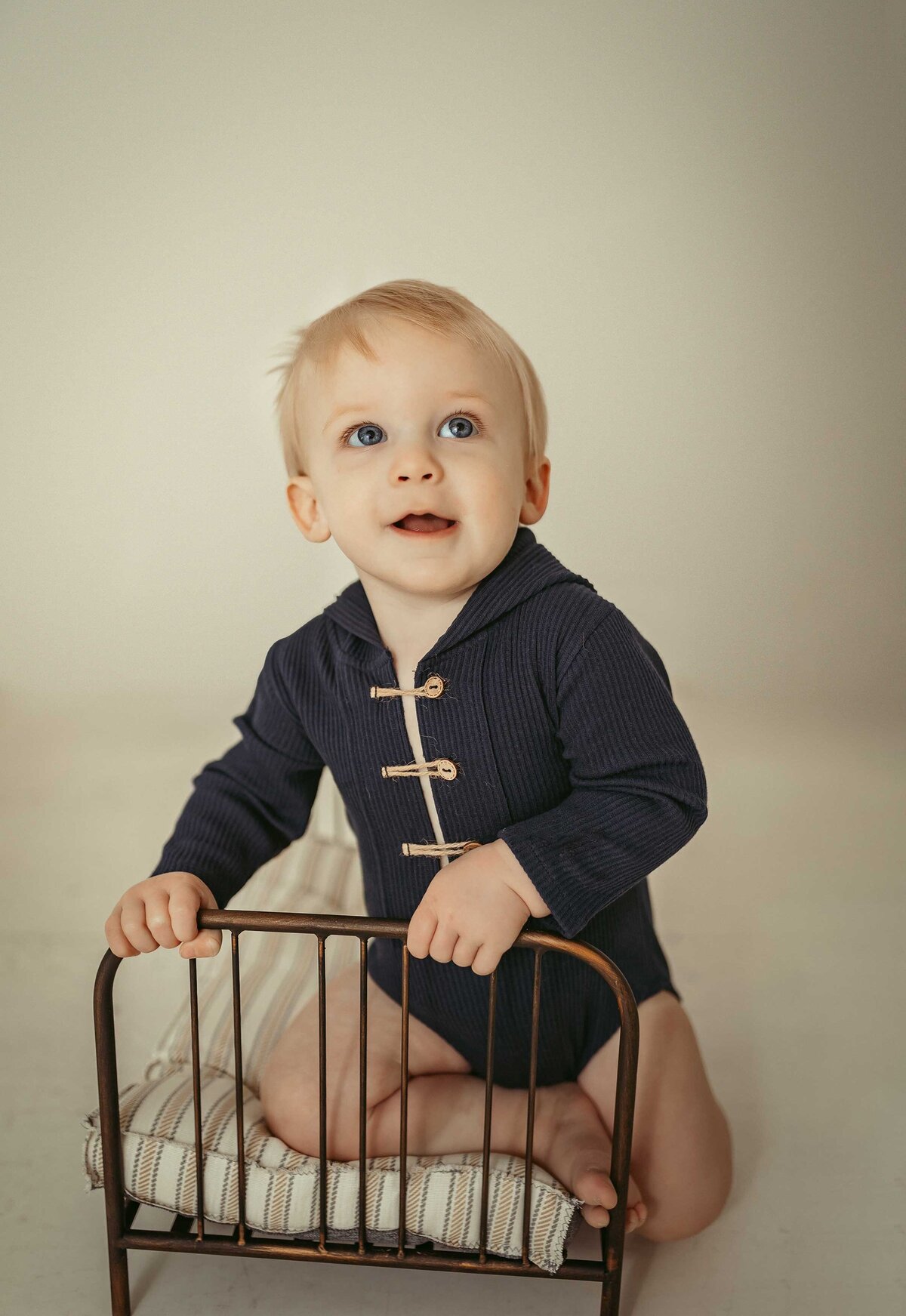 boy kneeling on a small toy crib wearing a dark navy outfit