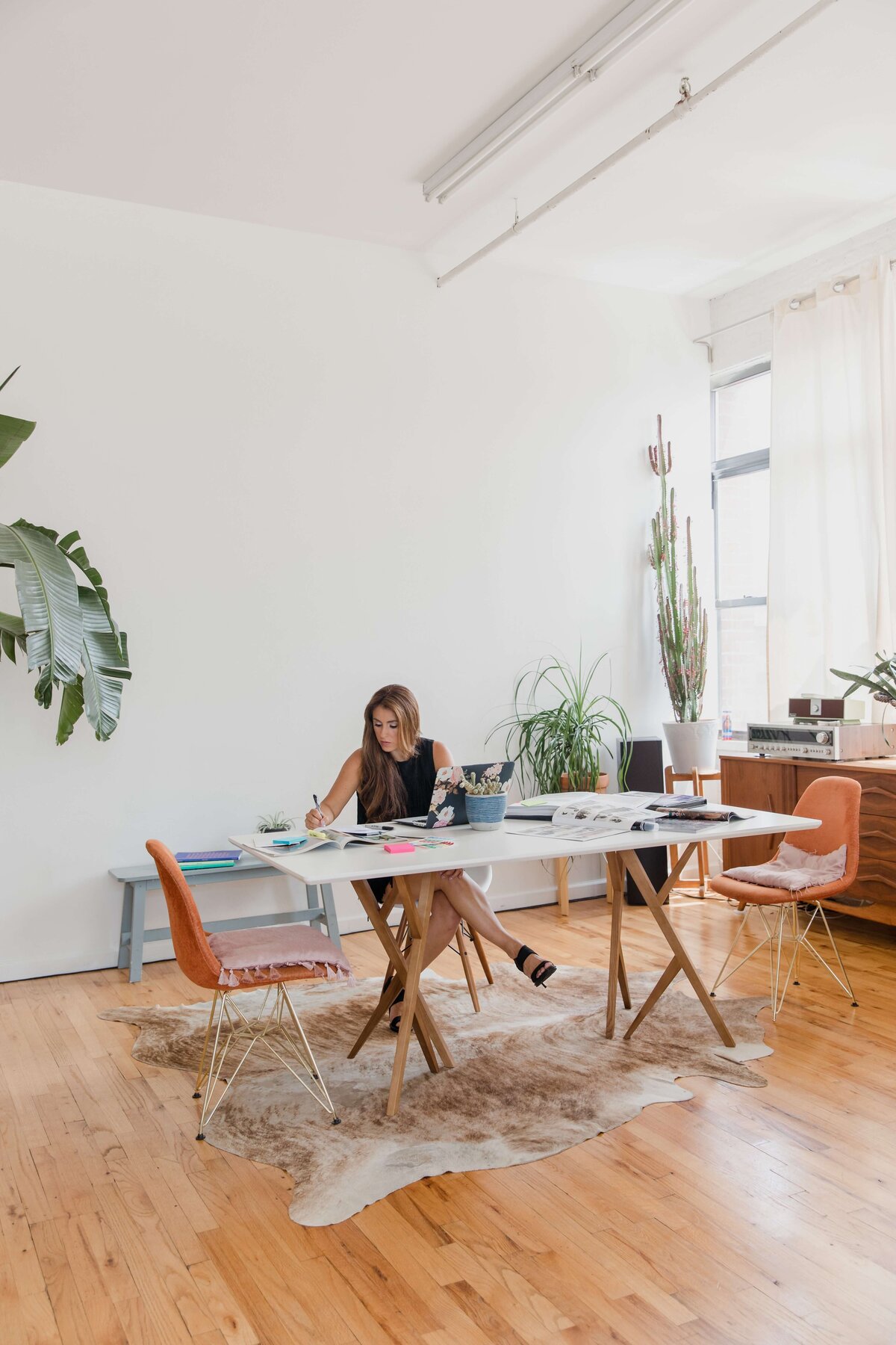 A woman works in an airy minimal office with decorative feminine touches like a fur rug and floral accents