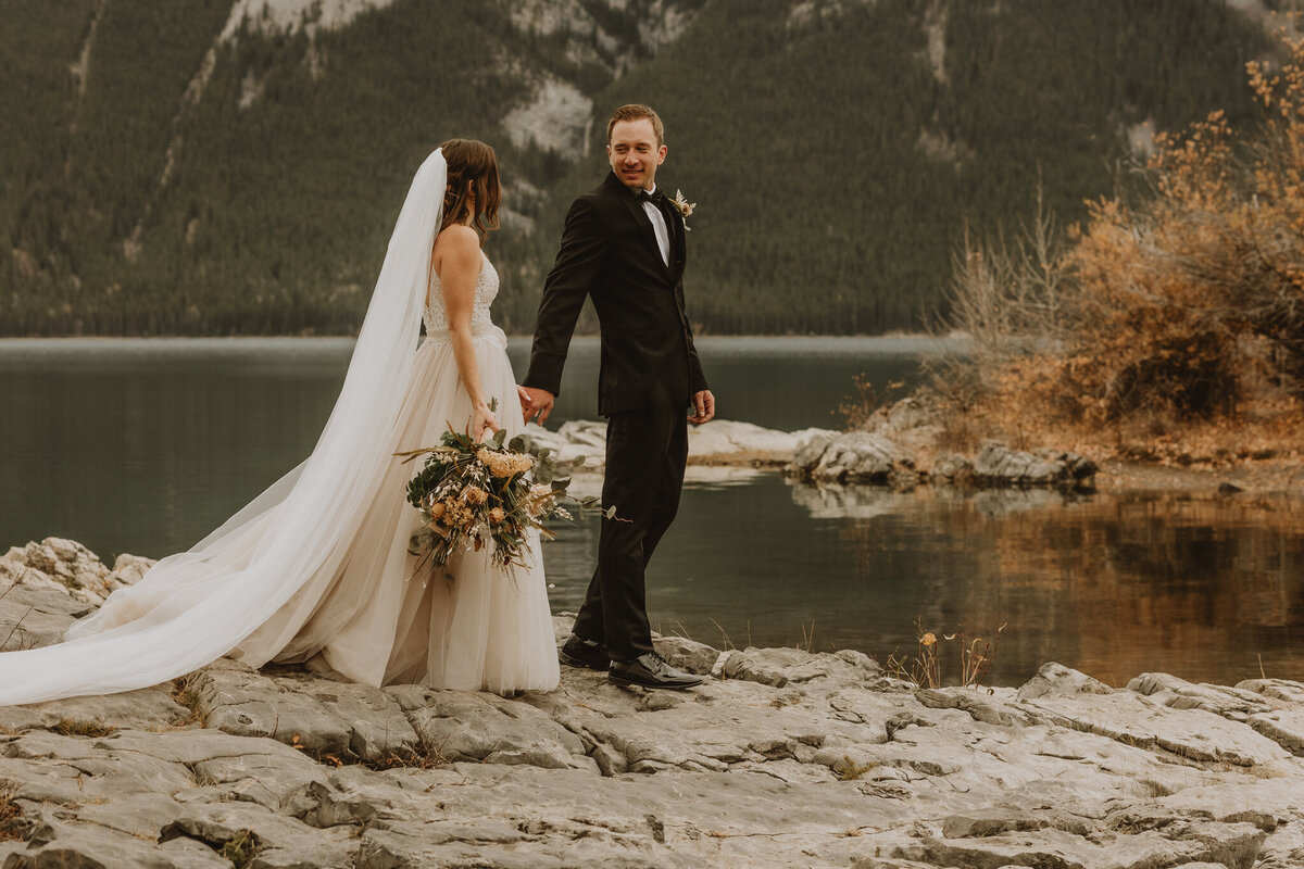 Bride and groom walking on the rocks at lake minnewanka , Banff