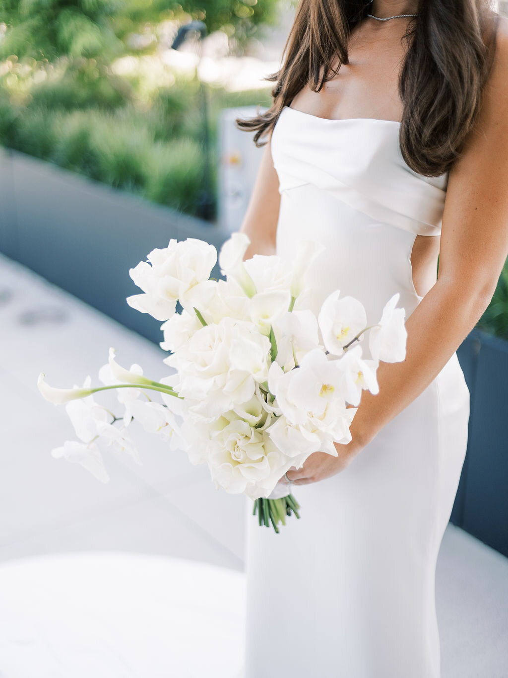 A close-up of the bride’s modern white gown and her elegant bouquet of white flowers.