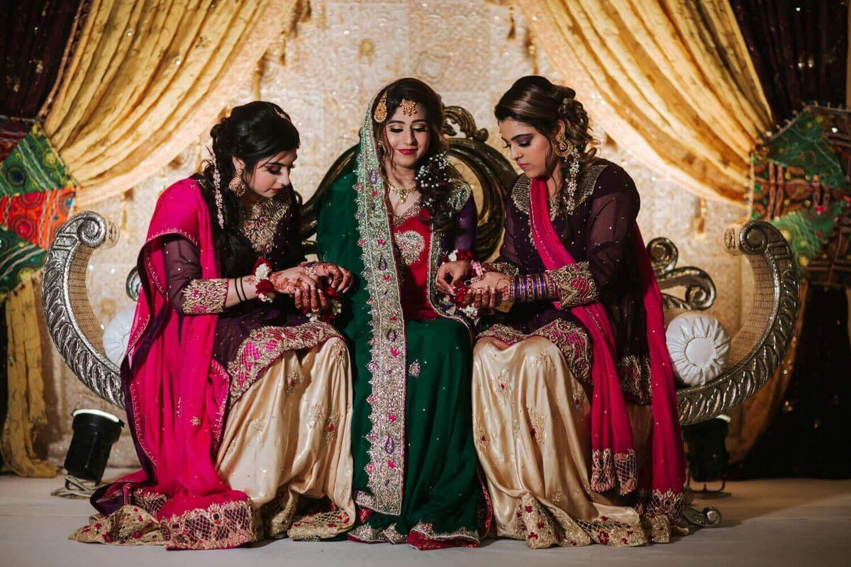 South Asian bride sitting on stage with her two sisters enjoying a moment of solitude before the Halud night.