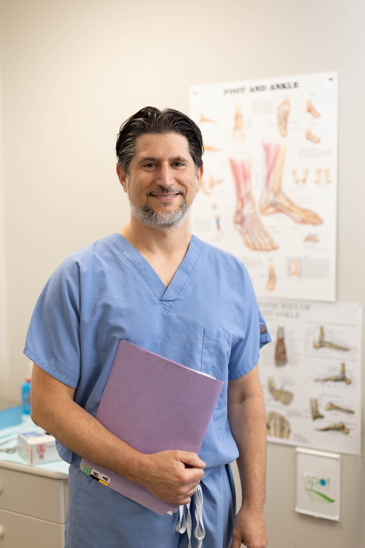 Podiatrist standing smiling, with a poster of feet behind him