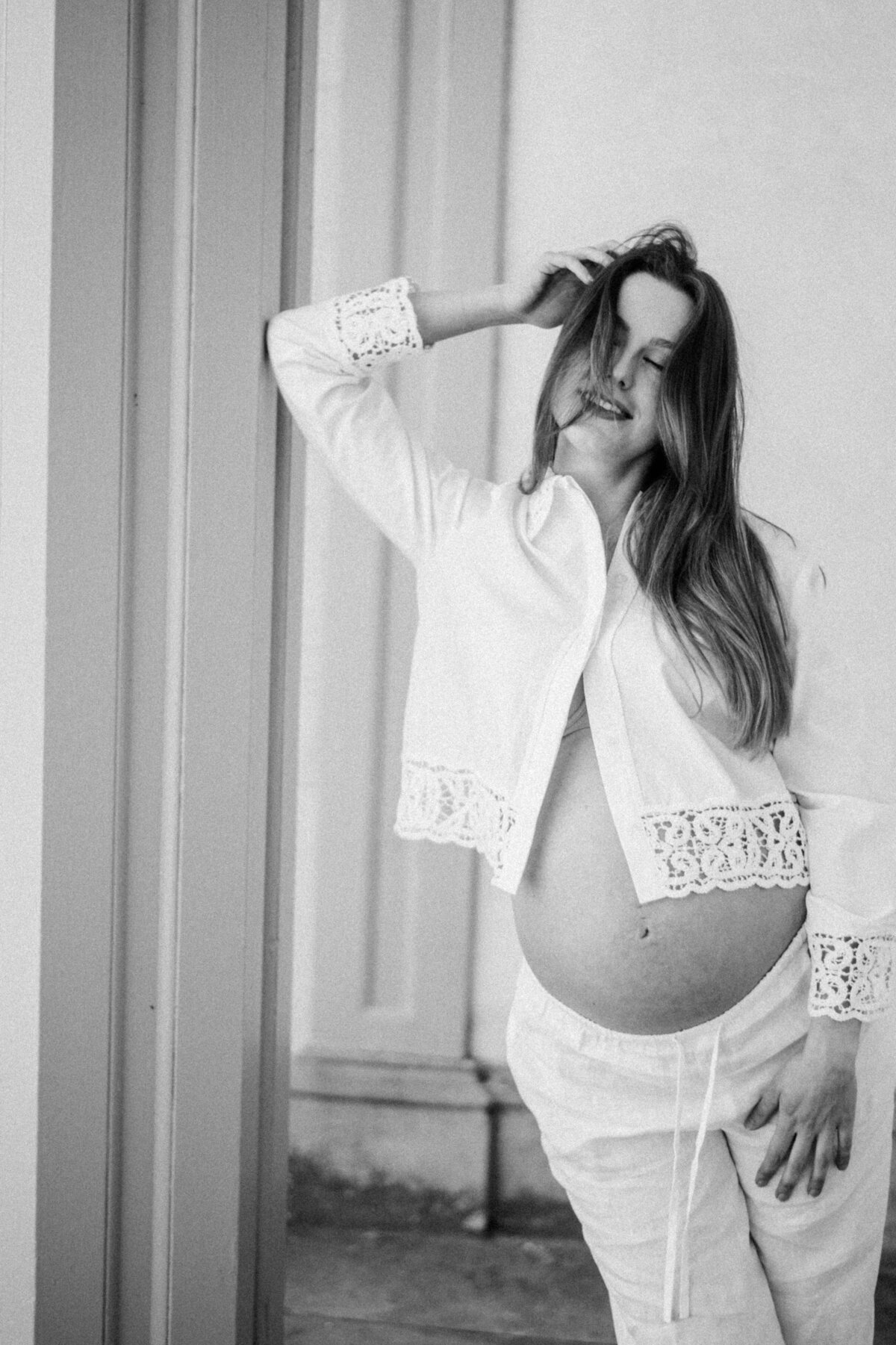 Editorial black-and-white maternity portrait of a poised mother-to-be in heels, framed by architectural columns