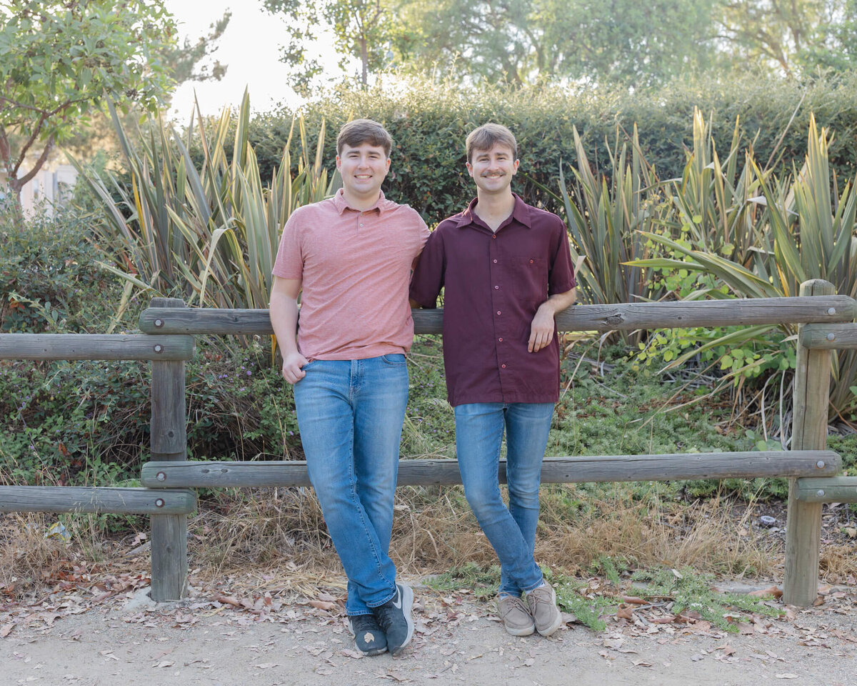 Two brothers wearing different shades of red with blue jeans smiling at the camera with their arms around each other at Citrus Ranch Park in Tustin.