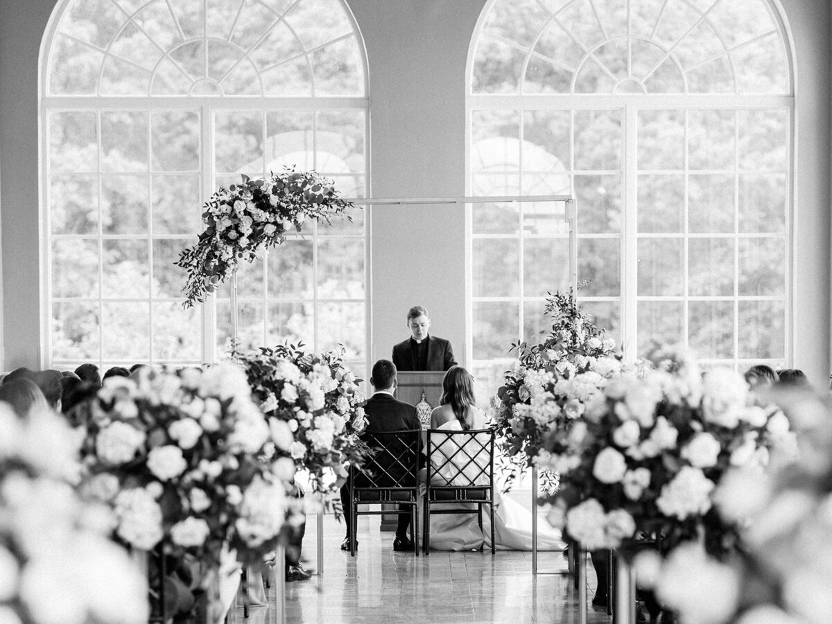 A black and white photo of the ceremony lined with florals down the middle