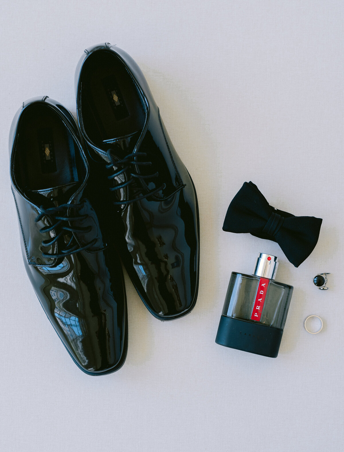 Grooms shiny black shoes with bowtie and cologne