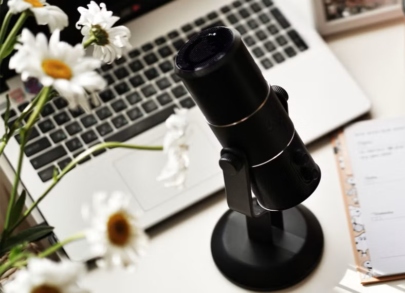 A microphone, daisies, and a laptop in my workspace, representing the personalized and unique services I offer to support your healing and growth.