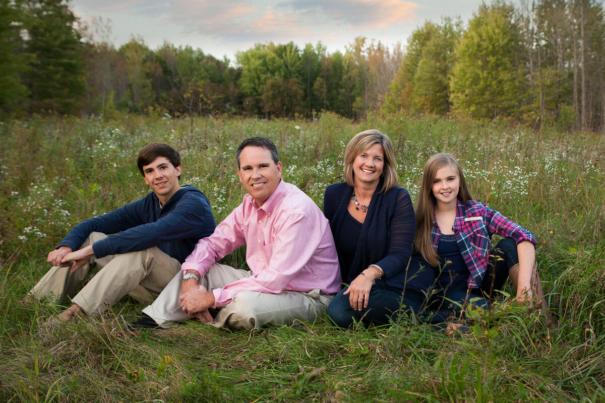 Early fall family portrait sitting in a green field with long grass