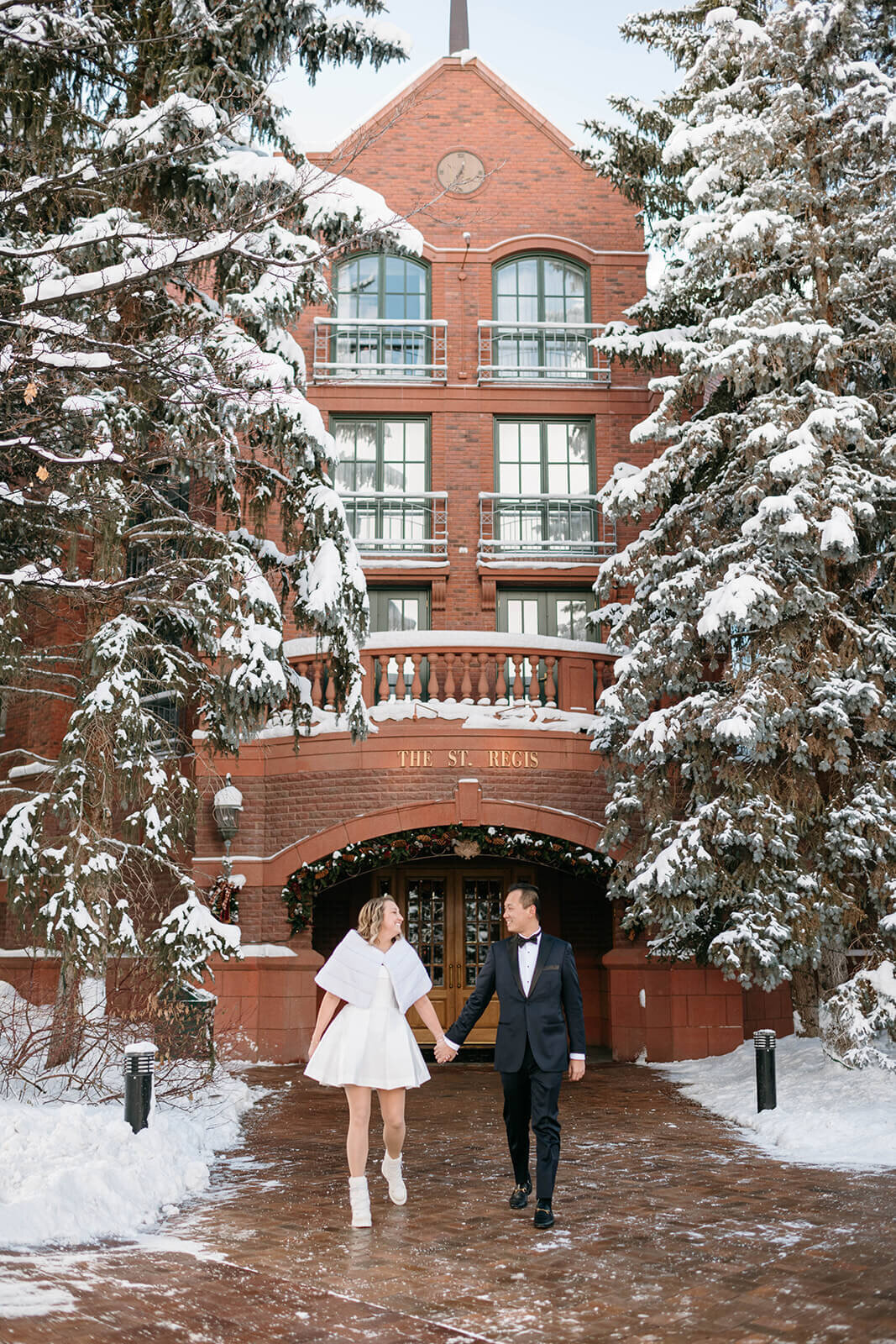 Bride and groom standing at the entrance of The St. Regis Aspen, framed by its iconic architecture and elegant surroundings.