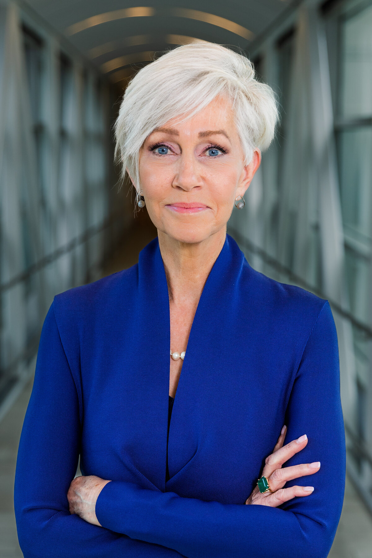 woman wearing a blue outfit standing arms crossed in front of  a modern urban glass bridge during portraits session