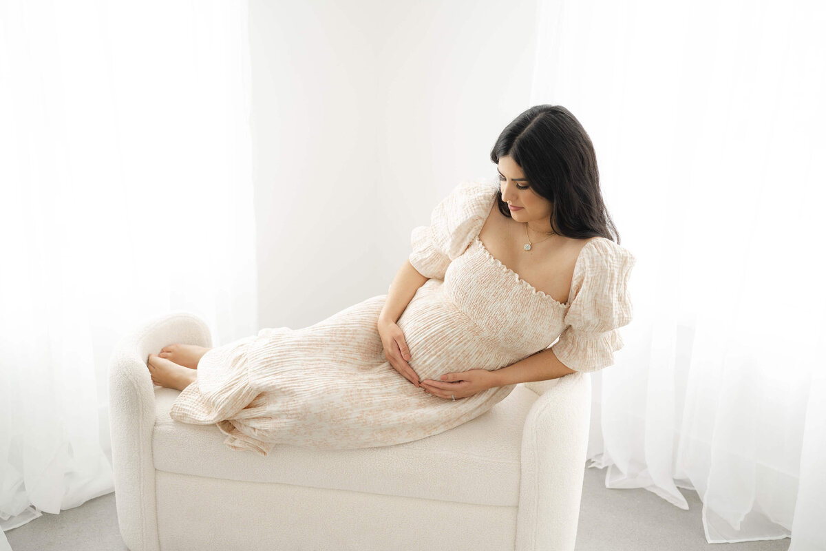 mom to be resting on a bench holding her bump in a beautiful natural light room