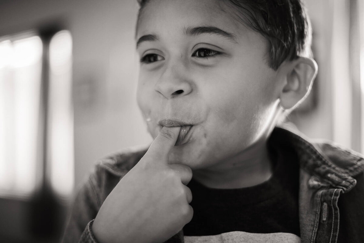 A boy smiles as he licks the cake batter off of his finger.